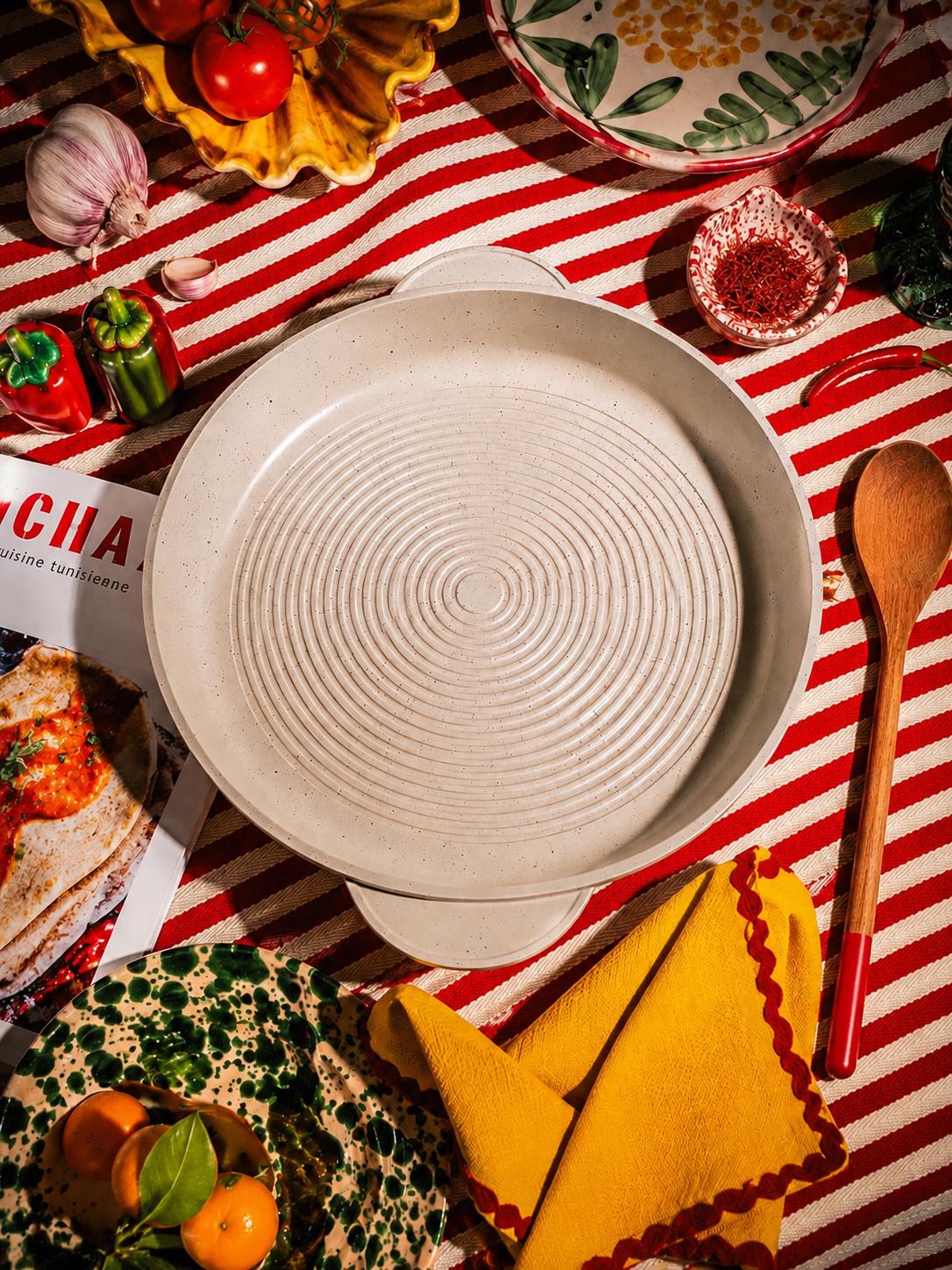 Tajine-Pan posée sur une nappe rayée rouge et blanche, entourée d’ingrédients colorés